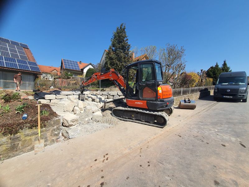 Kubota-Minibagger an einer Hofeinfahrt mit Trockenmauer