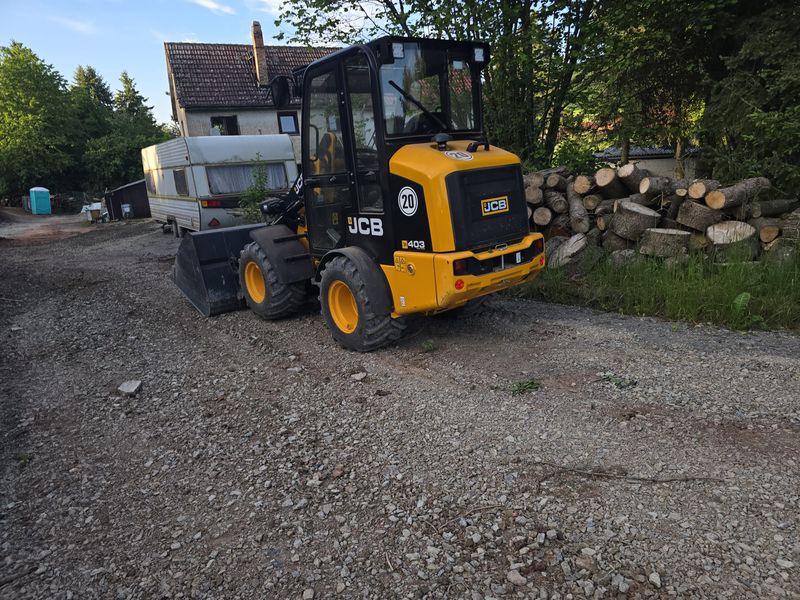 JCB-Radlader auf befestigtem Hofplatz neben Holzlager